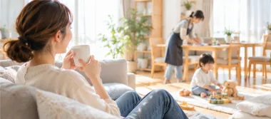 ソファでくつろぐ女性と、奥で家事をする家事代行スタッフ